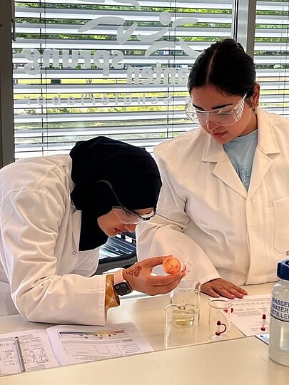 Zwei Schülerinnen in Laborkitteln experimentieren mit Schutzbrille