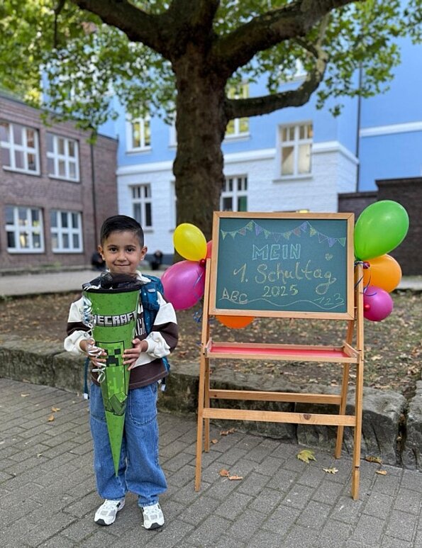 Amir Ocak mit Schultüte vor einer Tafel mit bunten Luftballons