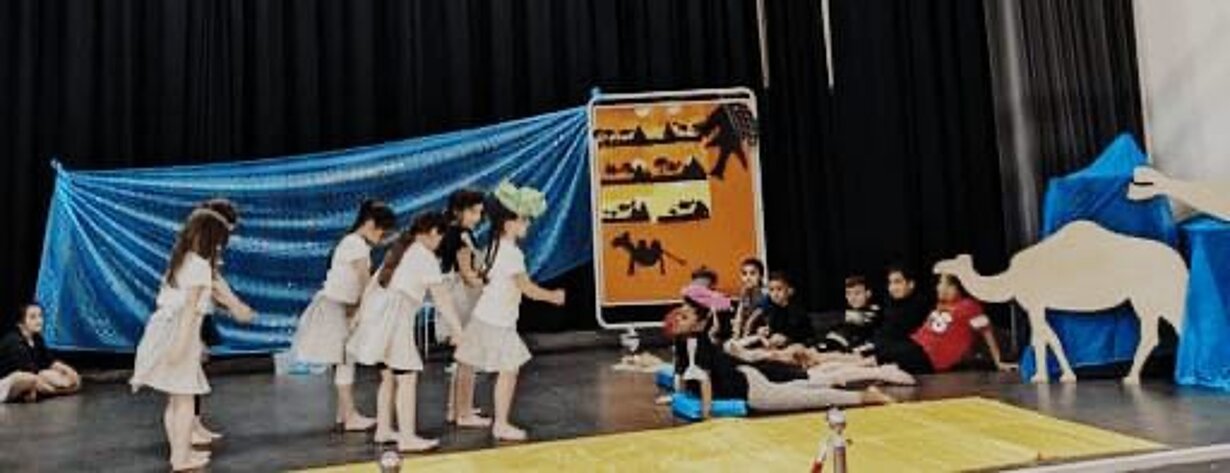 Vorschulkinder spielen ein Theaterstück mit Kamel-Kulisse auf der Bühne