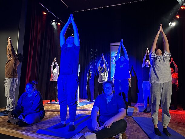Schülerinnen und Schüler zeigen Yoga-Übungen in blauem Bühnenlicht