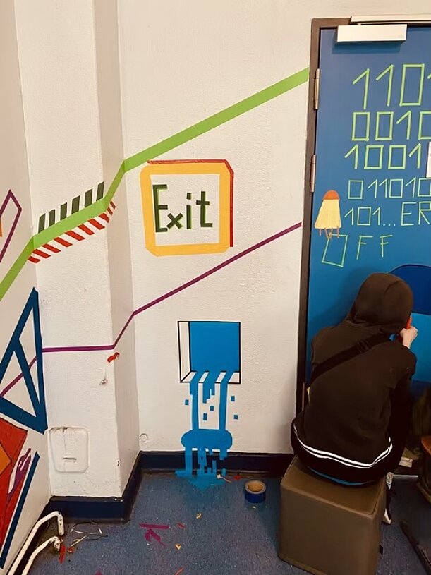 Schülerin gestaltet Tür mit Binärcode und Exit-Schild aus Klebeband