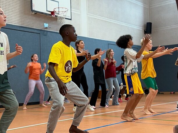 Kinder und Jugendliche tanzen gemeinsam in der Sporthalle mit NAFSI-Tänzern