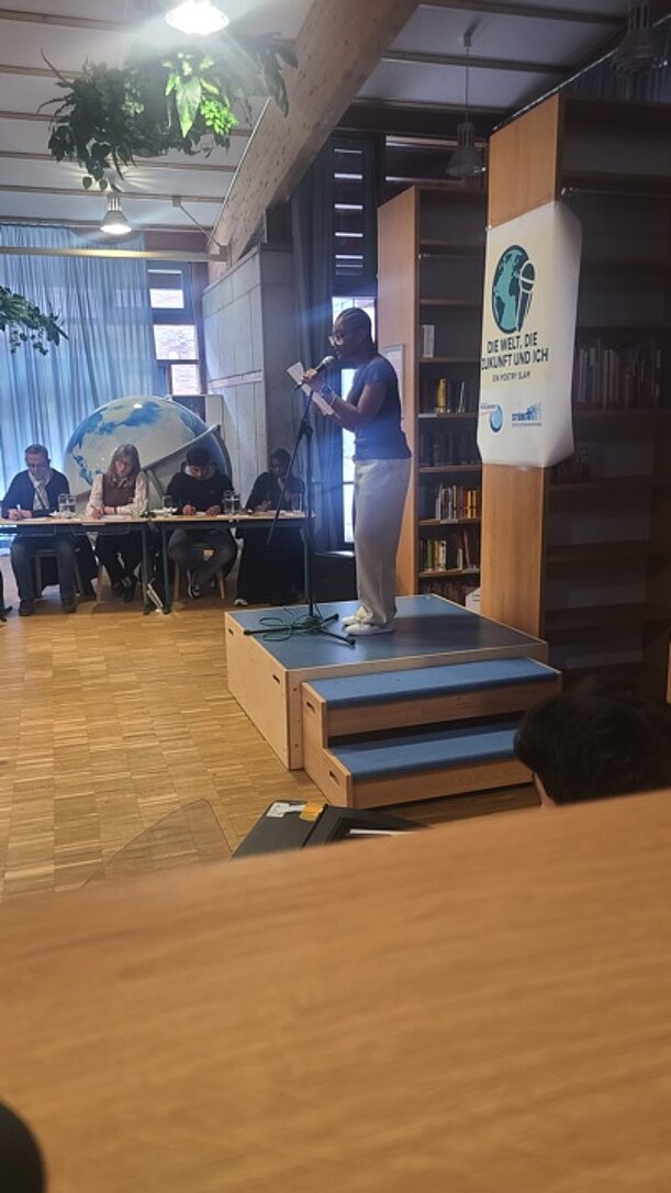 Slammerin trägt auf der Bühne vor, am Tisch sitzt die Jury