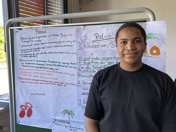 Muhammad steht vor einem Plakat zum Thema Palmöl