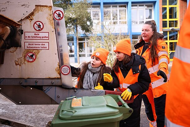 Kinder in orangen Westen werfen Müll in ein Müllfahrzeug