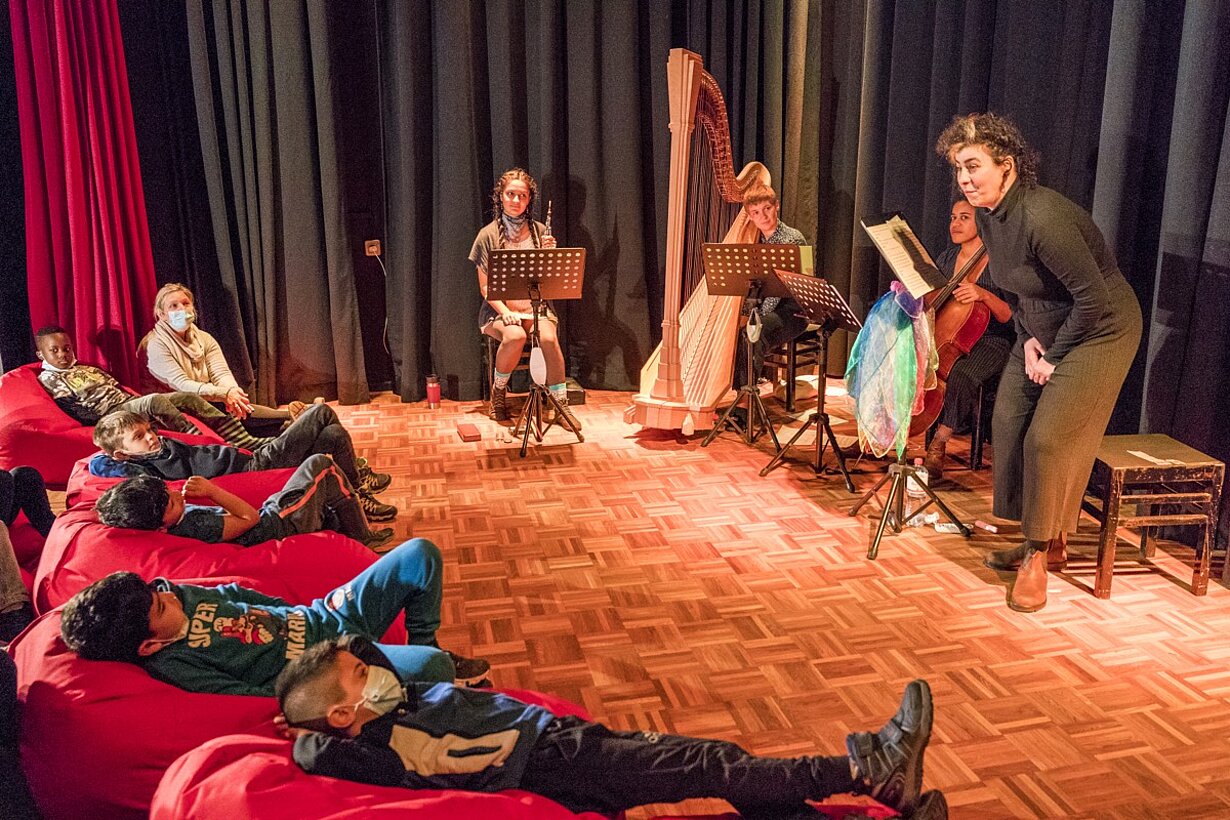 Kinder liegen auf roten Sitzsäcken beim Kinderkonzert mit Harfe und Cello in der Aula