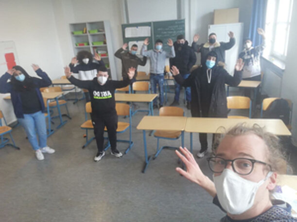 Jugendliche strecken im Klassenraum die Arme hoch, vorn eine Trainerin mit Maske