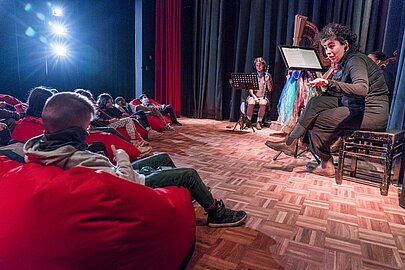 Musikerin mit Notenpult spielt vor liegenden Kindern im Scheinwerferlicht
