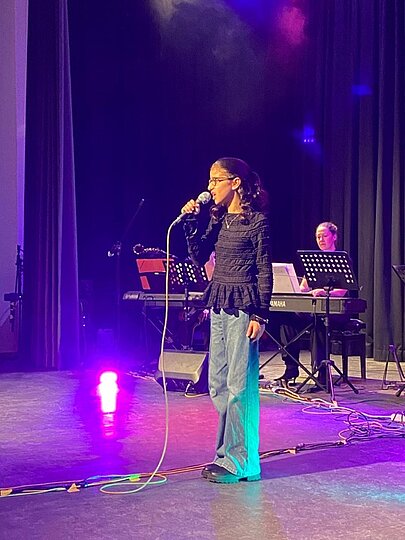 Sängerin in schwarzem Top und Jeans unter violettem Licht