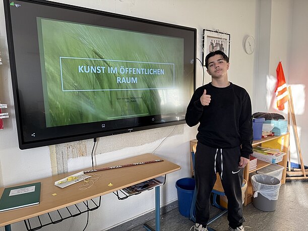 Schüler neben Bildschirm mit Präsentation „Kunst im öffentlichen Raum“