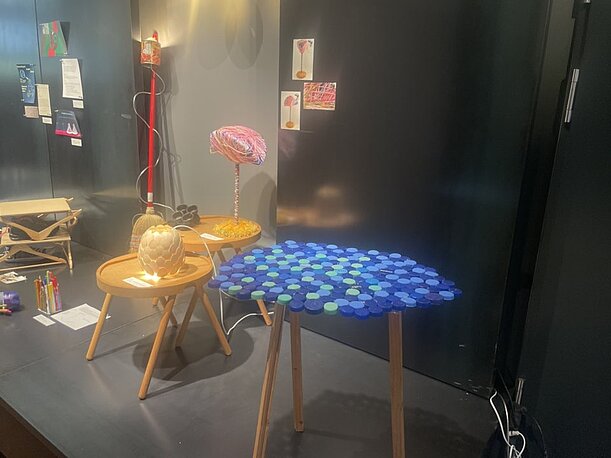 Tischentwurf mit blauer Deckelplatte neben Lampen in der Ausstellung