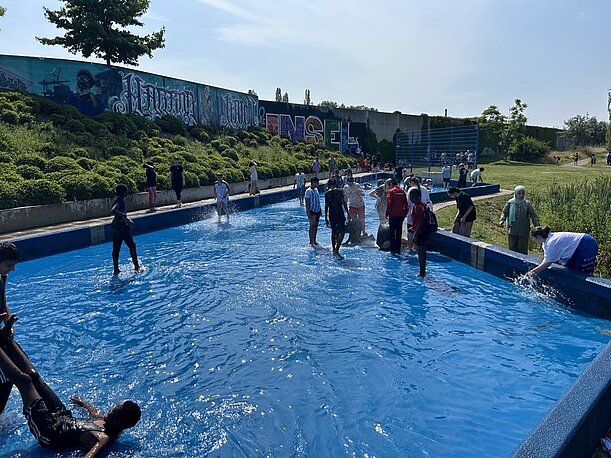 Schülerinnen und Schüler waten durch ein flaches Wasserbecken im Park