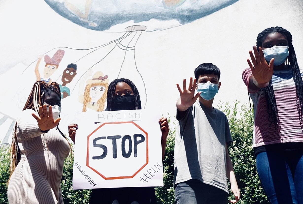Bandfoto: vier Jugendliche mit „Stop“-Schild und erhobenen Händen