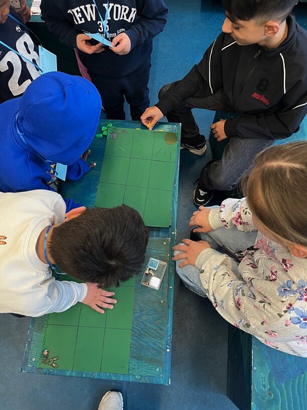 Kinder untersuchen am Forschertag etwas auf einer grünen Unterlage