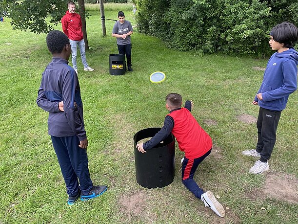 Kinder werfen Frisbees in schwarze Tonnen auf der Wiese