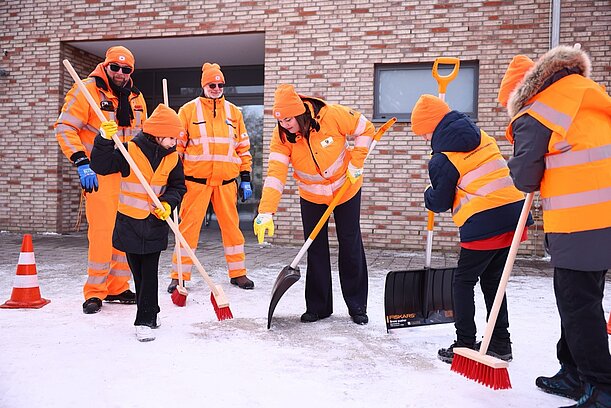 Kinder und Stadtreinigung in Orange fegen Schnee auf dem Schulhof