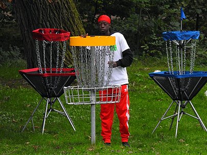 Trainer in Rot zwischen bunten Discgolf-Körben auf der Wiese