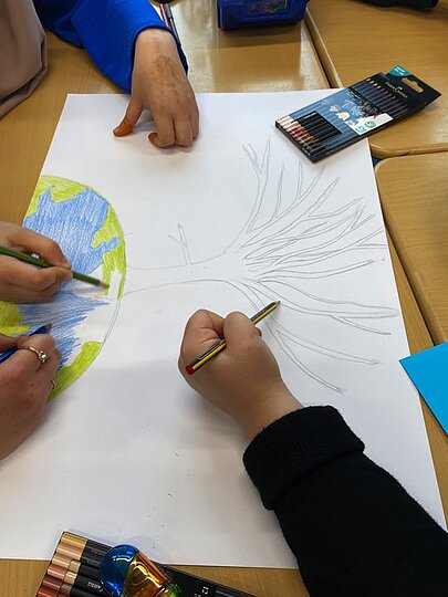 Kinderhände malen eine Weltkugel auf ein großes Blatt Papier