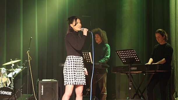Sängerin im karierten Rock vor grünem Vorhang mit Keyboarderin