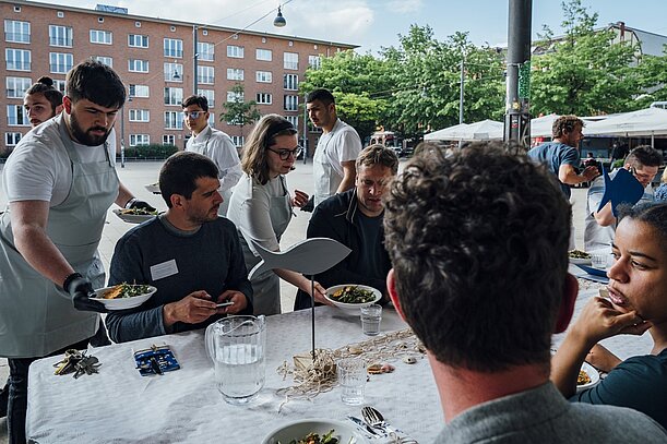 Gäste essen an gedeckter Tafel beim Stadtteildinner auf dem Stübenplatz