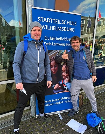 Zwei Läufer vor einem Roll-up der Stadtteilschule Wilhelmsburg beim Insellauf