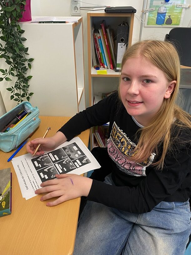 Emily zeichnet am Tisch Comicbilder auf ein Arbeitsblatt
