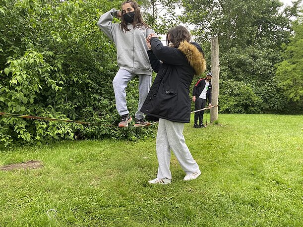 Schülerin balanciert mit Hilfestellung auf einer Slackline