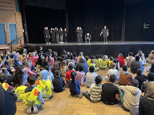Grundschulkinder sitzen vor der Bühne beim Theaterstück der Klasse 12a