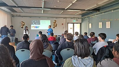 Publikum im Saal verfolgt Ehrung vor Leinwand und goldenen Ballons