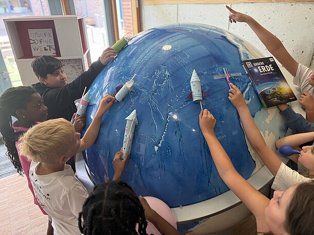 Kinder platzieren Papierraketen an einem großen blauen Globus
