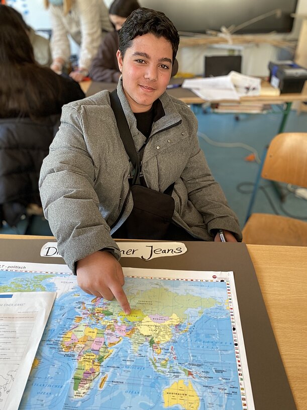 Schüler zeigt auf einer Weltkarte den Weg einer Jeans