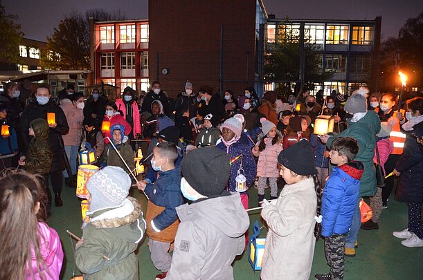 Viele Kinder und Eltern mit Laternen auf dem Schulhof am Abend