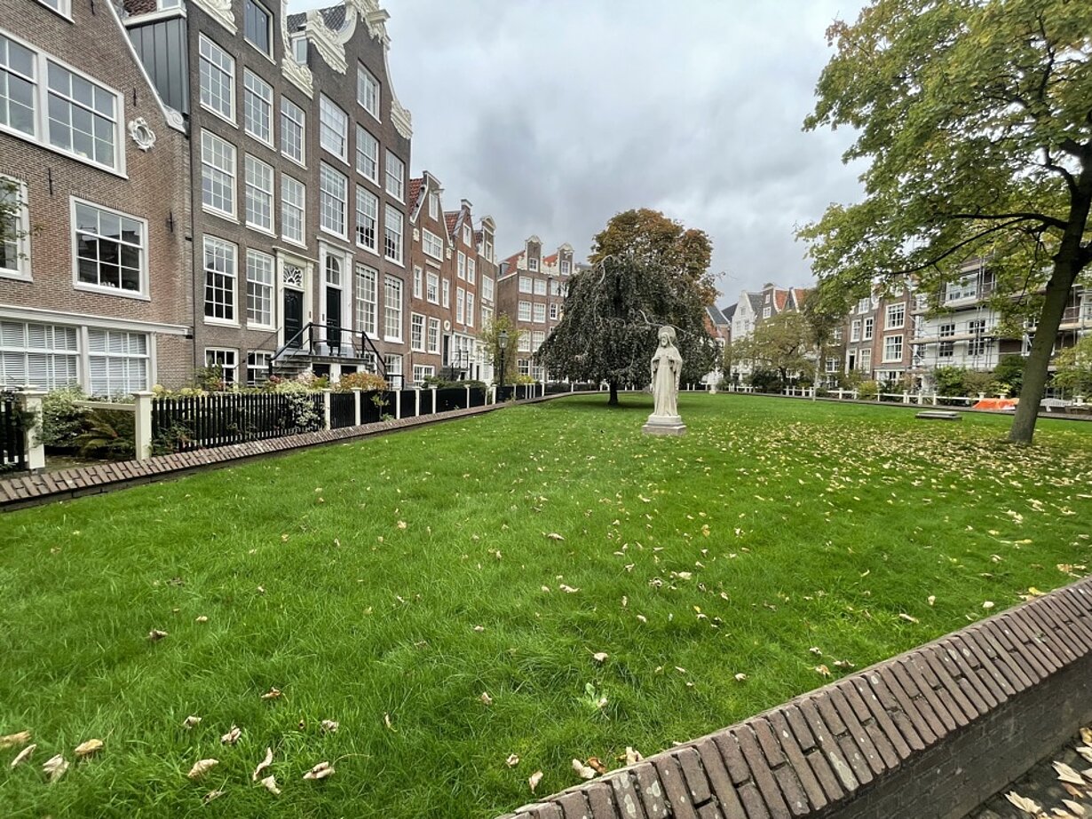 Rasenfläche mit Statue und alten Häusern im Begijnhof Amsterdam