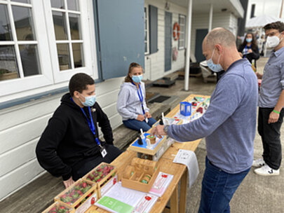 Jugendliche und Erwachsene an einem Stand mit Pflanzkästen beim Spreehafenfest