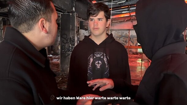 Filmstill der 10e: Jugendliche im Gespräch in einem dunklen Raum mit Untertitel