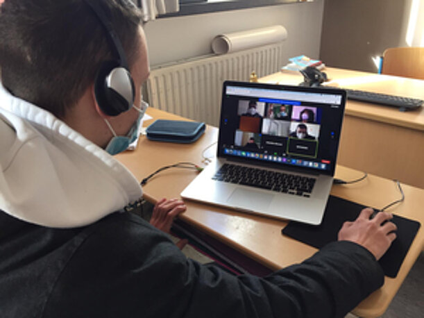 Schüler mit Kopfhörern im Videocall am Laptop beim MUT-Workshop