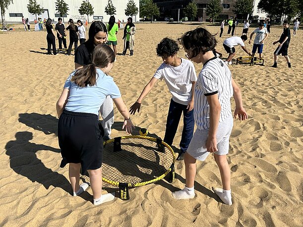 Kinder spielen Spikeball auf einem Sandplatz