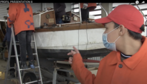 Schüler in orangefarbener Jacke erklärt Arbeiten an einem Boot