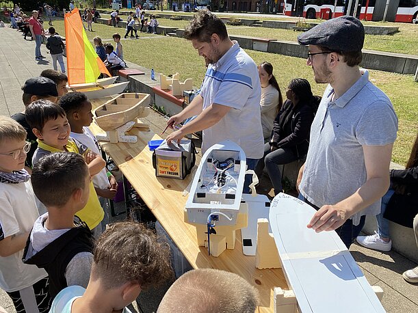 Lehrer zeigen Kindern selbstgebaute Boote auf einem Holztisch