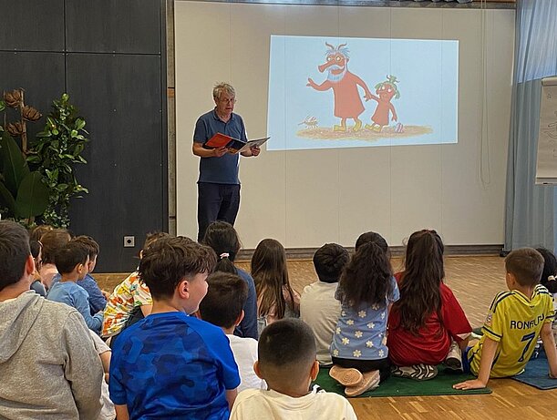 Axel Scheffler liest vor Leinwand mit Grüffelo-Bild vor sitzenden Kindern