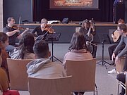 Schülerinnen und Schüler hören einem Streicherensemble im Saal zu