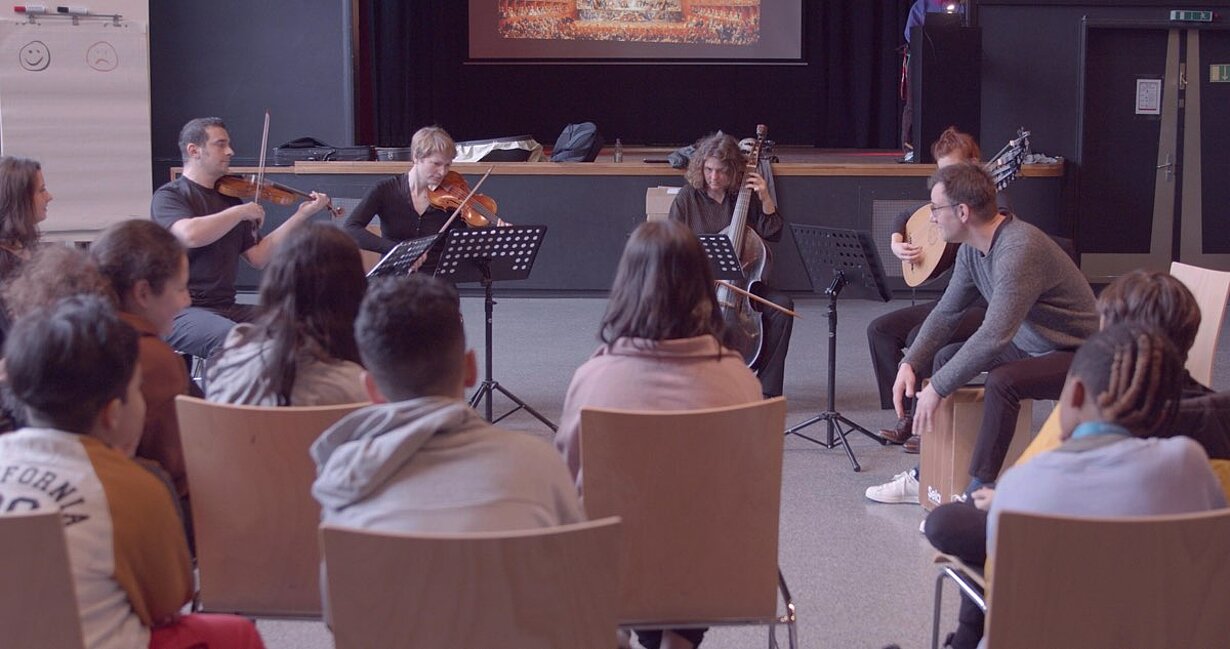 Schülerinnen und Schüler hören einem Streicherensemble im Saal zu