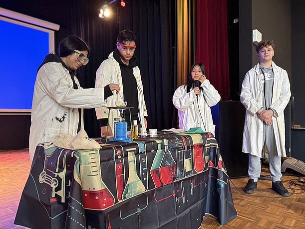 Klasse 9b in Laborkitteln führt die Herstellung von Lippenbalsam vor