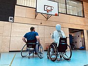 Basketballtrainer im Rollstuhl zeigt Schülerin den Positionswurf auf den Korb