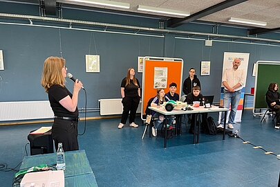 Katja Schlünzen begrüßt mit Mikrofon die Teilnehmenden beim WRO-Wettbewerb