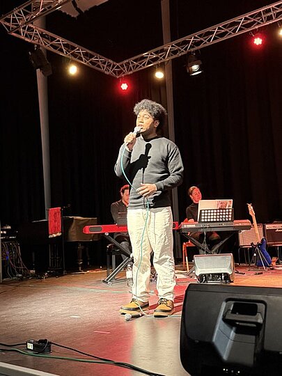 Sänger mit Mütze und weißer Hose auf rot beleuchteter Bühne beim Voice