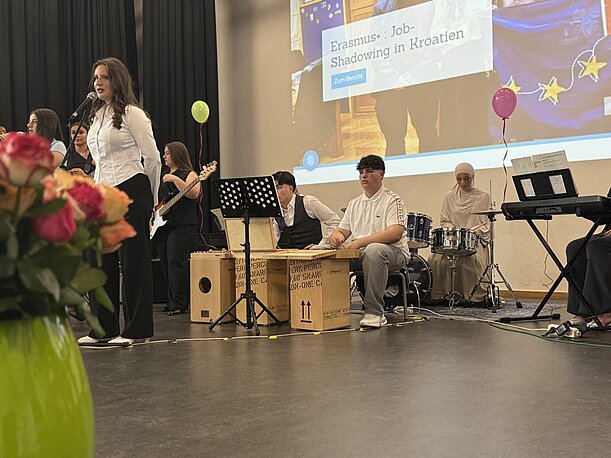 Sängerin mit Band auf der Bühne vor Leinwand mit Schulprojekten