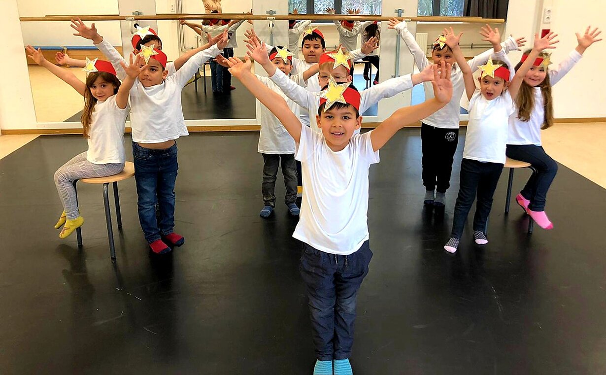 Vorschulkinder mit Sternkronen tanzen mit ausgestreckten Armen