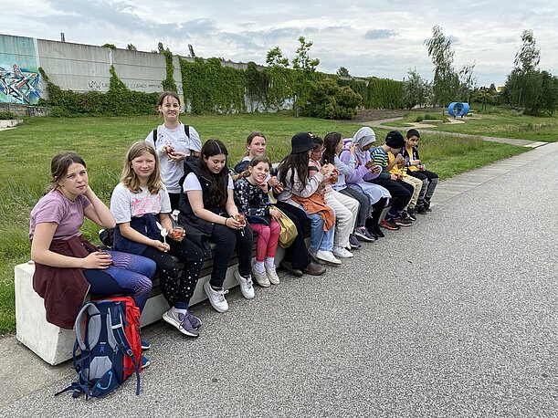 Jugendliche sitzen in einer langen Reihe auf einer Mauer am Weg