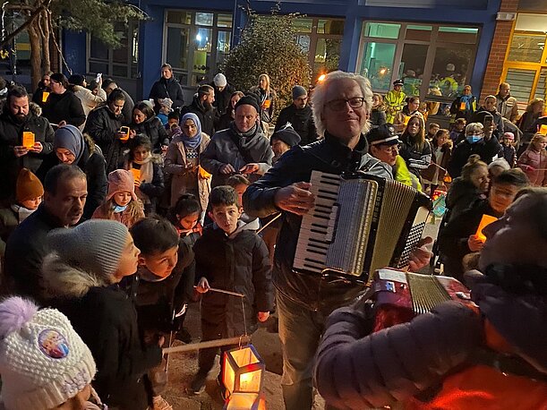 Kinder und Eltern singen mit Akkordeonbegleitung vor dem Laternenlauf